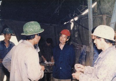 1985年7月，温家宝(中)在辽宁锦西盘道沟金矿区调研时在机台与工人交谈。