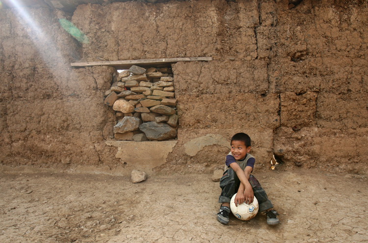 图文:古路村小学生拿着足球坐在操场泥墙边