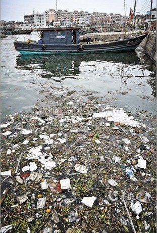练江出海口，大片的垃圾铺在水面上。不远处就停泊着久不出海的渔船。