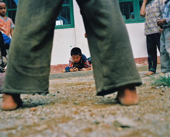 图文:学生光脚在教室外的地上玩着弹球游戏