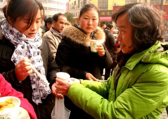 1月22日，不少志愿者纷纷加入到“送粥奶奶”的队伍。这是台湾籍志愿者陈淑芳（右）在给排队购票的外来务工人员送粥。　新华社发（李孟龙摄）