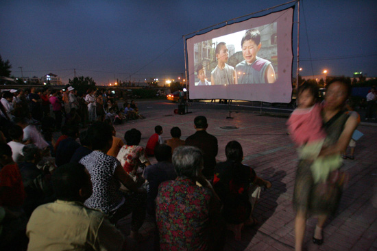 夜幕降临,移动电影放映车前大幕拉起,数百人围坐在广场上.