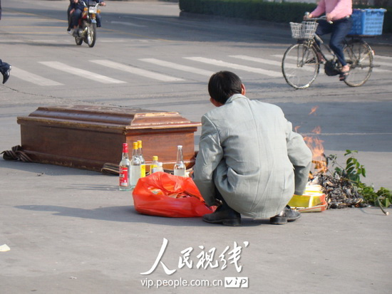 广东东莞虎门北栅一街头,身穿灰布西装男子正在给一口棺材焚烧纸钱