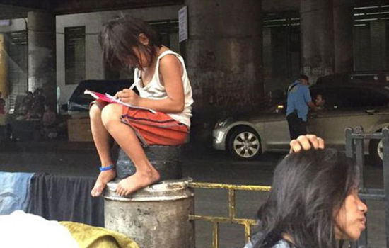 了一名叫做冈萨雷斯的小女孩赤脚坐在大街防护栏墩上弯腰做作业的照片