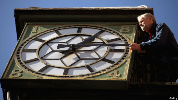 A man moves the hands of an old town clock.