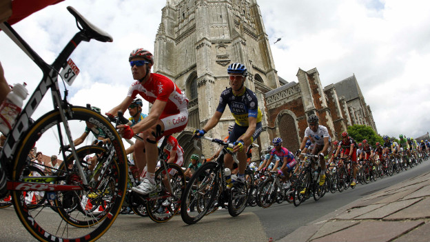 Riders in the Tour de France cycle past the church of Aire-sur-la-Lys 