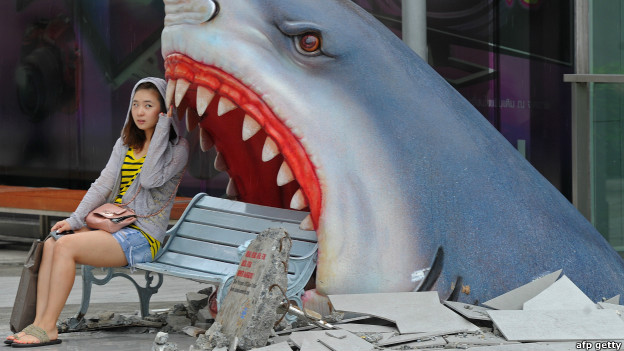 A tourist sits next to a large art display of a shark at a shopping mall in Bangkok. 