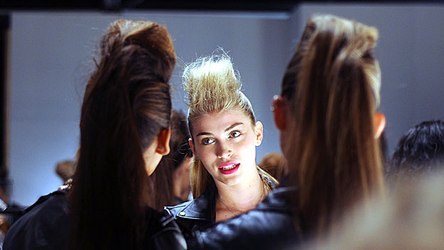 Three models with tall haircuts talk backstage at London Fashion Week. 