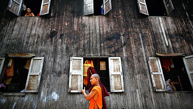 A Buddhist monk carries his robe as another looks out of the window of their monastery.