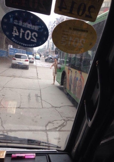 照片中,男子全裸一丝不挂,并张开双手拦停公交,倚住车头.