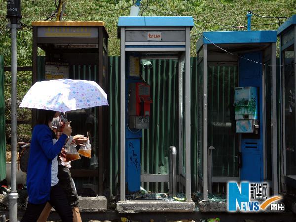5月21日,在曼谷本盖地区,两名行人走过一排遭破坏的公用电话亭.